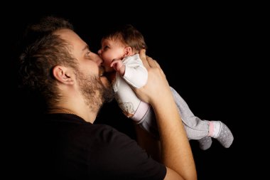 Siyah tişörtlü yakışıklı kaslı adamın stüdyo portresi. Siyah arka planlı şirin bir bebeğin ellerinde. Aile, aşk ve mutluluk kavramı.