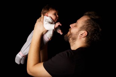 Siyah tişörtlü yakışıklı kaslı adamın stüdyo portresi. Siyah arka planlı şirin bir bebeğin ellerinde. Aile, aşk ve mutluluk kavramı.