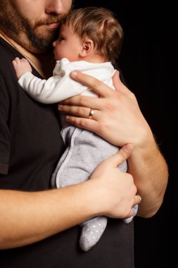 Siyah tişörtlü yakışıklı kaslı adamın stüdyo portresi. Siyah arka planlı şirin bir bebeğin ellerinde. Aile, aşk ve mutluluk kavramı.