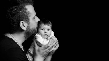 Siyah tişörtlü yakışıklı kaslı adamın stüdyo portresi. Siyah arka planlı şirin bir bebeğin ellerinde. Aile, aşk ve mutluluk kavramı.