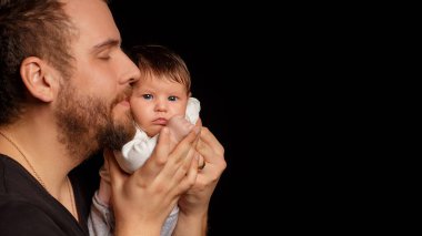 Siyah tişörtlü yakışıklı kaslı adamın stüdyo portresi. Siyah arka planlı şirin bir bebeğin ellerinde. Aile, aşk ve mutluluk kavramı.