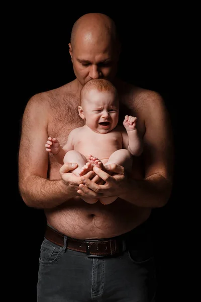 父亲抱着一个新生的儿子 吻了吻他 一个秃头的男人 全身赤裸 4个月大的婴儿 背景是黑色的 — 图库照片