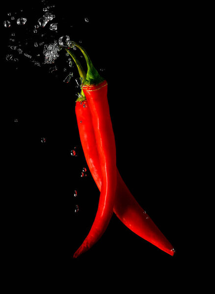 two pods of red chili peppers in water. Hot Peppers and bubbles of water on a black background.