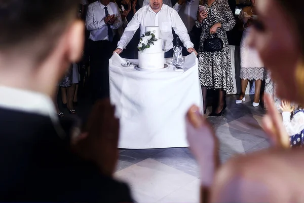 the waiter takes out a wedding cake for the bride and groom in the hall with guests.