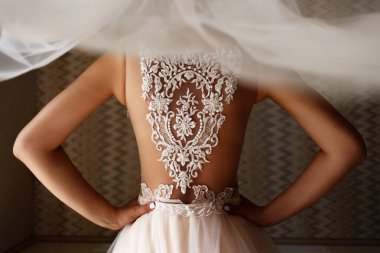 Gelin sırtı kameraya dönük duruyor. Bir kızın sırtında peçe ve dantel. Kadın kemerin üstünde el ele tutuşuyor..