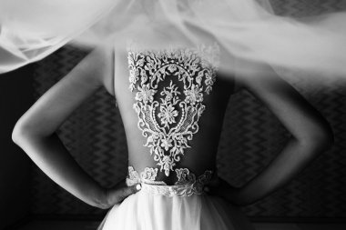 Gelin sırtı kameraya dönük duruyor. Bir kızın sırtında peçe ve dantel. Kadın kemerin üstünde el ele tutuşuyor..