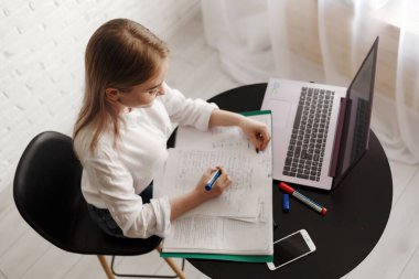 Beyaz bluzlu genç sarışın kız odada çalışıyor. Belgeleri ve dizüstü bilgisayarı var. Evde çalış. Kadın, elinde belgelerle masada otururken kameraya bak..