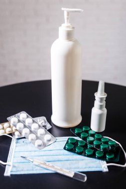 Soğuk algınlığı ve virüs semptomları için tıbbi konsept. Koruyucu maskeli haplar, termometre ve boğaz spreyi ve antiseptik içeren şişeler..