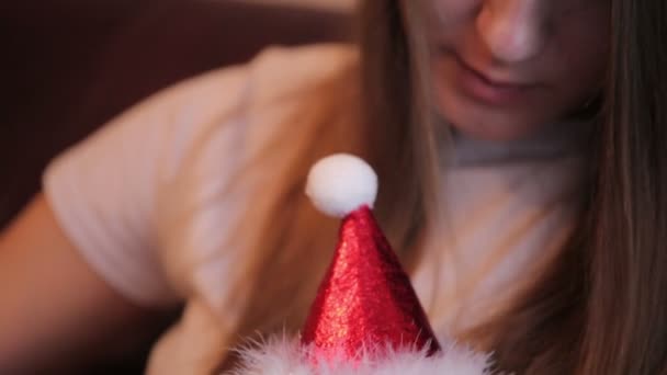 Κορίτσι χαϊδεύει και χαϊδεύοντας της βρετανική γάτα με μεγάλα μάτια σε Χριστούγεννα καπέλο και λευκό μαντίλι στο σπίτι. — Αρχείο Βίντεο