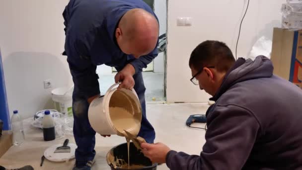 建设者浇灌 揉搓和称重胶水 施工搅拌机在工作 男人倒胶水 浓重的液体混在桶里 — 图库视频影像