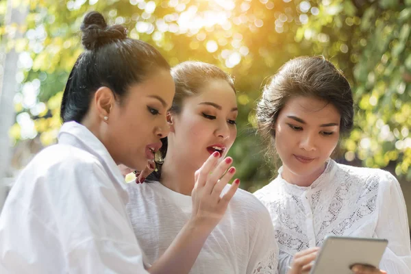 Tres hermosas mujeres sentadas en un parque con una tableta . —  Fotos de Stock