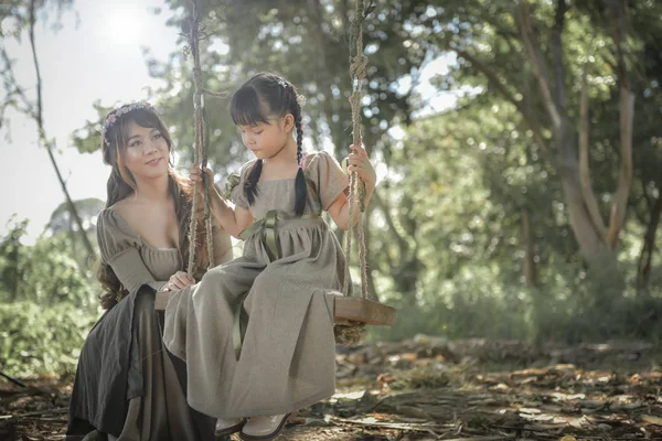 La hermana se balancea a su hermana bajo los árboles sombríos en th —  Fotos de Stock