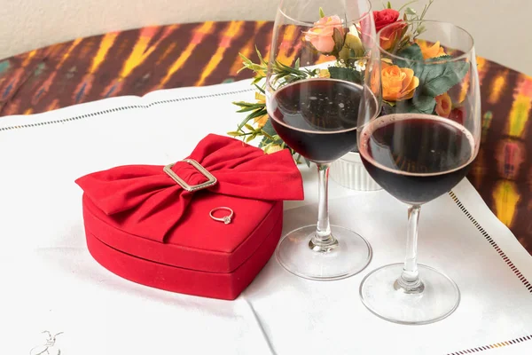 Copa de vino y caja en forma de corazón con anillos de boda en la mesa — Foto de Stock