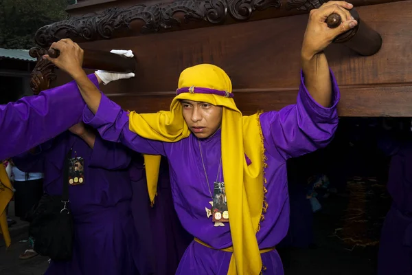 若い男が紫と黄色のローブを身に着けているイースターのお祝いをグアテマラのアンティグアの聖週の間にフロート (anda) を運ぶ. — ストック写真