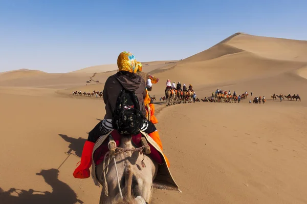 Τουρίστες σε ένα καμήλα τροχόσπιτο στους αμμόλοφους γύρω από την πόλη του Dunhuang, στον αρχαίο δρόμο του μεταξιού, στην Κίνα. — Φωτογραφία Αρχείου