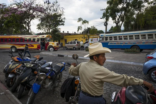 Street scene in the city of Antigua, in Guatemala, with a local man in the foreground and two buses on the background, in Guatemala. — Stock Photo, Image