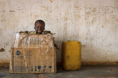 Nhacra, Republic of Guinea-Bissau - January 28, 2018: Portrait of a young boy playing in a card box in the town of Nhacra in Guinea Bissau, West Africa clipart