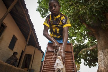 Nhacra, Republic of Guinea-Bissau - January 28, 2018: Young African boy washing his clothes in a washing board in the town of Nhacra in Guinea Bissau, West Africa clipart