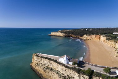 Güzelim Praia da Senhora da Rocha 'nın (Sinyora da Rocha Sahili), Armacao de Pera, Algarve, Portekiz yakınlarındaki kayalıklardaki beyaz şapeli gösteren hava aracı fotoğrafı.