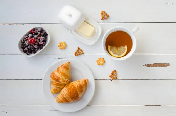 Desayuno de croissants calientes, mantequilla, té y grosellas en mesa de madera. Puesta plana — Foto de Stock