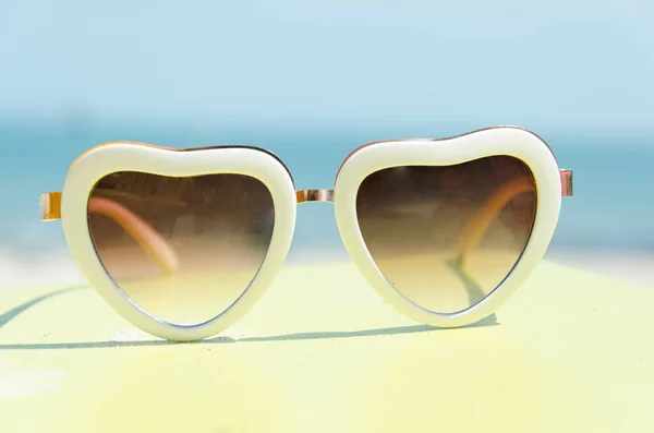 Mode Sonnenbrille Herz auf gelbem Ständer mit blauem Meereshintergrund — Stockfoto