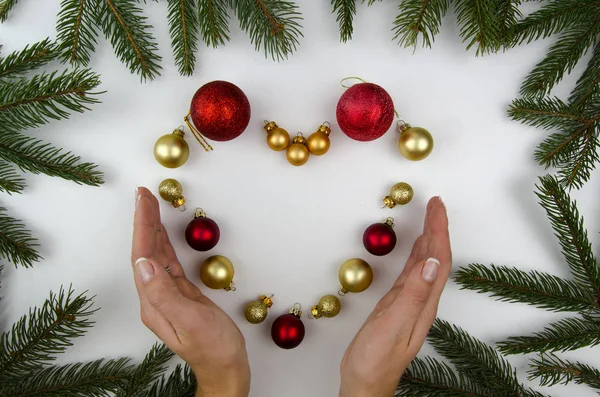 Cuore fatto di decorazioni natalizie e mani di woomen. Bianco sfondo palle di Natale. piatto lay — Foto Stock