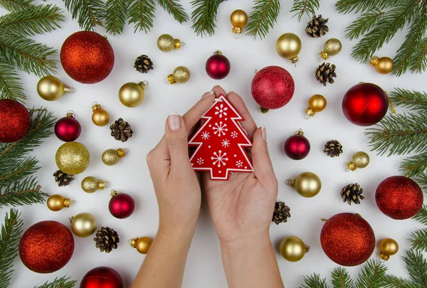 Női kéz tartja a vörös karácsonyfa játék. Karácsonyi összetétele készült arany és piros labdákat a karácsonyfa, a kúpok és a fenyő ágak. Karácsonyi háttér. Téli lapos — Stock Fotó