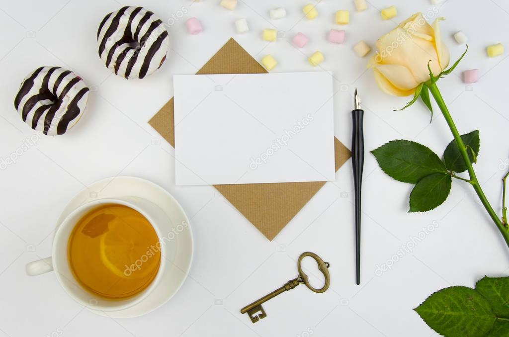 A creative mans desktop with a rose, sweets, donuts, marshmallows , cup of tea., envelope, empty letter and a calligraphic fountain pen for writing the best wishes or romantic letter.