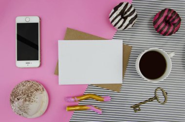 Cep telefonu ve kraft envelopeon geometrik pastel arka sayfada boş kağıt mockup pembe çizgili. Cap kahve, anahtar ve tatlı çörek yatıyordu, en iyi görünüm düz.