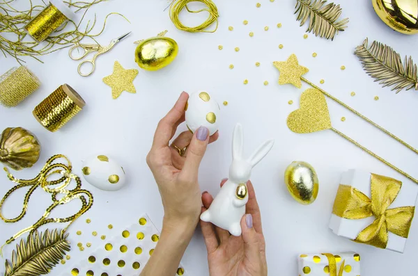 Festa da Santa Páscoa. A menina está segurando um coelho de Páscoa de porcelana e ovo de Páscoa branco decorado com círculos dourados. Composição plana . — Fotografia de Stock