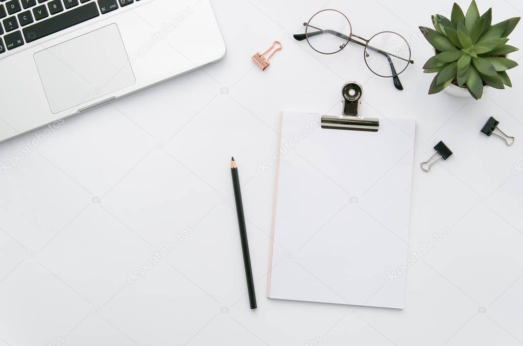 Home office workspace mockup with laptop, clipboard, green plant, notebook and eyeglasses, with copy space background. Flat lay, top view