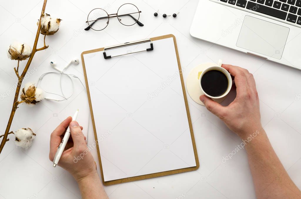 Home office workspace mockup with laptop, clipboard, notebook and accessories. Man holding a pen and coffee. Flat lay, top view