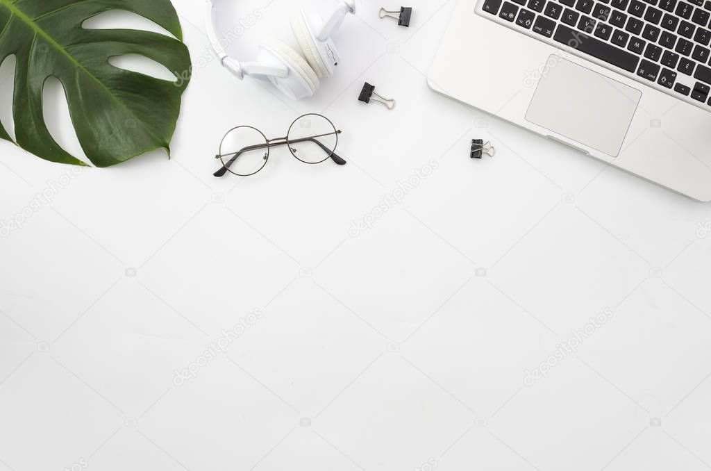 Flat lay, top view office table desk. Workspace with laptop, green palm branch, glasses, white headphones and clips on white background. Mockup