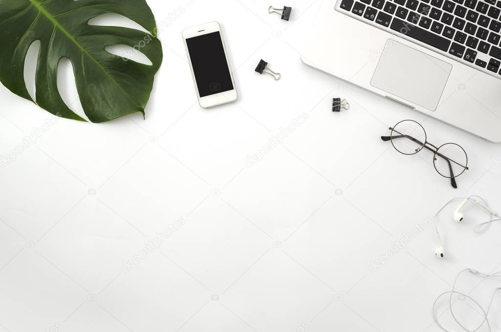 Workspace with laptop, mobile phone, green palm branch, glasses, white headphones and clips on white background. Mockup Flat lay, top view office table desk.
