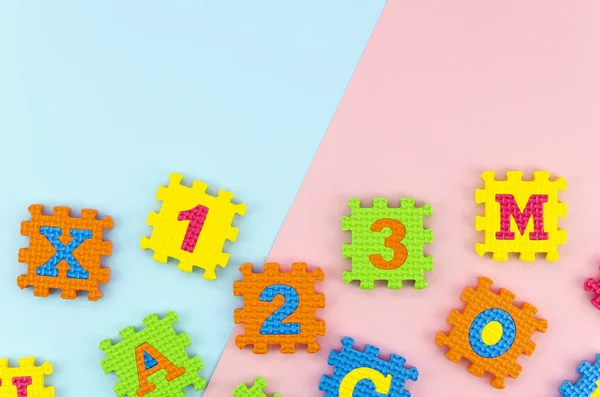 Flat lay Learning toys puzzle with numbers and letters on geometric blue and pink pastel background with copy space