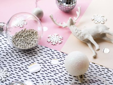 Tatil festivali natürmort konsepti: Pastel geometrik pembe ve beyaz arka planda Noel süsleri ve dekorasyonları. Parlak ve konfetili şeffaf cam top.