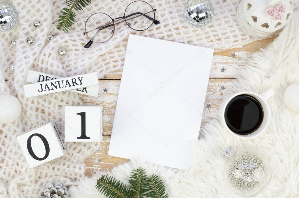 Flat lay mock up blank magazine cover with copy space with winter Christmas decoration, for branches on a cozy knitted background. Top view with glasses, cup of coffee and wooden calendar 01 January