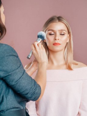 Sahne arkası makyözü pembe bluzlu, güzel sarışın bir mankenle uğraşıyor. Dikey çekim