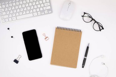 Gümüş bir bilgisayar klavyesi, boş akıllı telefon ekran modeli, sarmal not defteri ve malzemeleri olan üst katlı ofis masası. Mobil uygulama ekran görüntüsü konsepti
