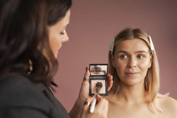 Makeup artist working with a blonde model in a beauty salon. Face sculpting. Contouring. Contour and highlight with Face Color Highlight, Sculpt and Blush Powder and brush