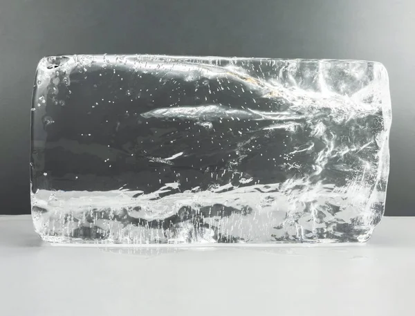 Cubo de fusión grande de hielo transparente sobre una mesa blanca y fondo gris. Hielo claro para esculpir — Foto de Stock