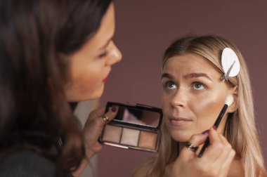 Profesyonel makyaj sanatçısı mükemmel ciltli güzel bir modelde yüz pudrasının nasıl kullanılacağını ve uygulanacağını gösteriyor. Barutla bir palet tutar