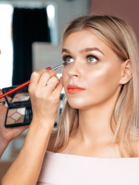 Sahne arkası makyaj sanatçısı, sarışın bir aktrisin kirpiklerini boyuyor. Yüz portresini kapat