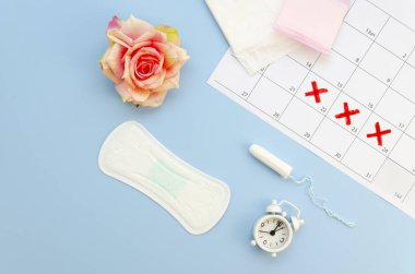 Eski moda kağıt menopoz takvimi tampon ve pedlerle düzdü. Gül çiçeği ve beyaz alarmlı saat ile üst görünüm bileşimi