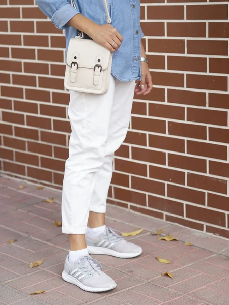 Una mujer elegante vestida con una camisa azul y calzones sostiene una bolsa. Calle urbana plano vertical sobre un fondo de pared de ladrillo rojo. Cuerpo recortado sin rostro — Foto de Stock