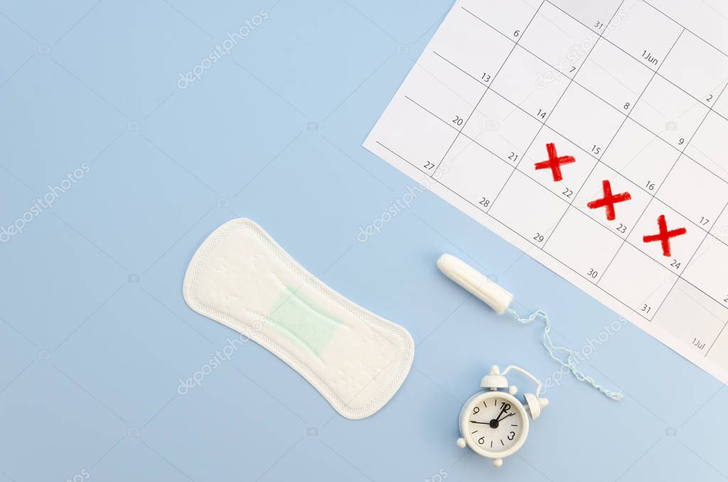 Flat lay female cycle calendar with menstrual pad, tampon and white alarm clock on a pastel background