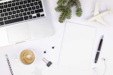 Beyaz bir masada, gümüş dizüstü bilgisayarı, kahve fincanı, uçak oyuncağı ve köknar dalıyla yazı için yeri olan boş kağıt liste modeli. Kış tatili konsepti