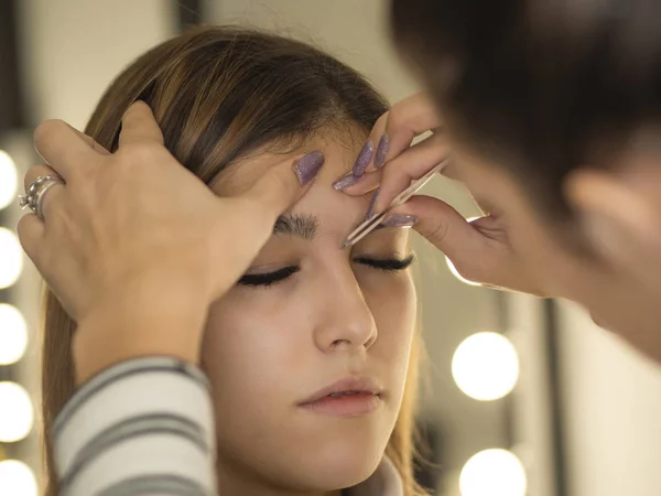 Beautician Master corrects shapes eyebrows in a beauty salon, makeup mirror on background