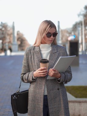 Soğuk bir sonbahar gününde beyaz bir dergi taşıyan beyaz ceketli sarışın beyaz bir kadın. Kapağı boş ve kahvesi de hazır. Kopyalama alanı ile modelleme