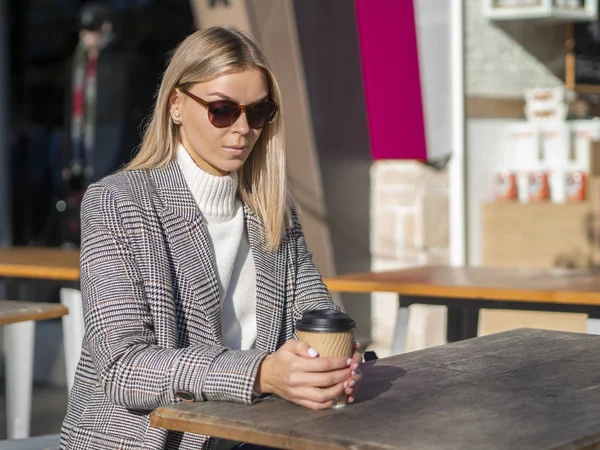 Mujer de negocios joven en abrigo sentado en la cafetería de la calle con café de la mañana. Tiempo frío — Foto de Stock